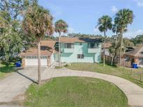 Charming two-story home with circular drive, attached garage, and mature palm trees enhancing the property's curb appeal at 2715 Pine Tree Dr, Edgewater, FL 32141