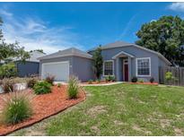 Charming single-Gathering home featuring well-kept lawn, mulched flowerbeds, a garage and a striking red front door at 411 Ryans Ridge Ave, Eustis, FL 32726