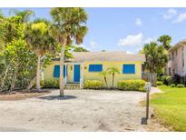 Charming yellow bungalow with blue shutters, palm trees, and a sandy front yard, offering a classic beach vibe at 821 Ocean Ave, New Smyrna Beach, FL 32169