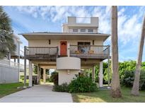 Charming two-story stilt home with a balcony, an orange door, and covered parking on a sunny day at 895 Catfish Ave, New Smyrna Beach, FL 32169