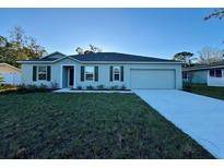 Newly constructed home with a green exterior, landscaping, and a large driveway at 3122 Kumquat Dr, Edgewater, FL 32141