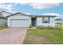 Charming single-story home featuring a well-manicured lawn, brick driveway, and a light blue exterior at 1489 Sea Glass Rd, Haines City, FL 33844