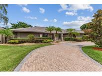 Luxury home exterior with a brick driveway, lush landscaping, and palm trees at 9227 Cypress Cove Dr, Orlando, FL 32819