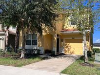 Two-story house with a yellow exterior, two-car garage, and landscaping at 9002 Majesty Palm Rd, Kissimmee, FL 34747