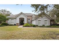 One-story house with gray stucco, stone accents, and a tile roof, showcasing a manicured lawn at 25515 Hawks Run Ln, Sorrento, FL 32776