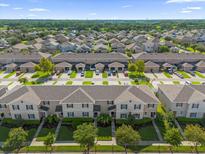 Expansive aerial view of a neighborhood showcasing rows of townhomes, landscaped streets, and verdant greenery, under a bright blue sky at 1625 Reflection Cv, Saint Cloud, FL 34771