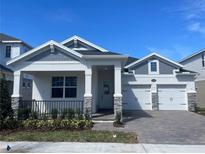 Charming new construction home featuring a welcoming front porch, brick driveway, and two-car garage at 16875 Muskgrass Dr, Winter Garden, FL 34787