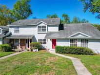 Traditional townhome features a well-manicured lawn, classic siding, a red front door, and mature trees at 1624 Rivers Edge Dr, Orlando, FL 32825