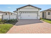 Exterior view of a house featuring a two-car garage with a brick driveway and manicured landscaping at 527 Kennedy Dr, Lake Alfred, FL 33850