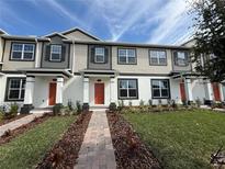 Charming townhome showcasing manicured landscaping, a brick walkway, and a welcoming orange front door at 791 Pilea St, Apopka, FL 32703