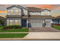 Two-story home with a three-car garage, brick paver driveway, manicured lawn and gray siding at 3198 Sailing Pier Ave, Winter Garden, FL 34787