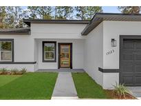 Modern home featuring a glass-paneled front door, white exterior, dark trim, and green lawn at 15123 Sw 61St Court Rd, Ocala, FL 34473