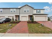 Two-story townhome with gray siding, brick paver driveway, and landscaping at 16387 Happy Eagle Dr, Clermont, FL 34714