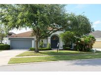Charming single-story home with a well-manicured lawn, mature tree, and gray garage door at 519 Lakescape Ct, Orlando, FL 32828