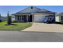 Charming single-story home boasts a well-manicured lawn, gray siding, and a convenient two-car garage, plus a golf cart at 4694 Monica St, The Villages, FL 32163