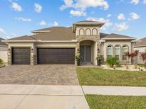 Beautiful home featuring a paved driveway and three-car garage, complemented by a stone-accented facade and lush landscaping at 489 Avila Pl, Howey In The Hills, FL 34737