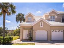 Charming townhouse featuring a two-car garage, white tile roof, and tropical landscaping at 7700 Carriage Homes Dr # 4, Orlando, FL 32819