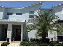 Modern two-story townhome features a red front door, a manicured lawn, and lush landscaping at 8943 Cabot Cliffs Dr, Davenport, FL 33896