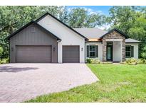 Charming single-story home with brick driveway, three-car garage, stone accents, and manicured lawn at 347 Mission Rd, Oviedo, FL 32765