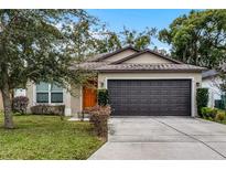 Tan house with orange door, dark brown garage door, and landscaped lawn at 1910 Rogers Ave, Maitland, FL 32751