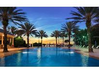 Stunning community pool lined with palm trees, lounge chairs, and a beautiful sunset at 7652 Whisper Way # 104, Reunion, FL 34747