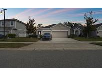 Charming single-story home featuring a two-car garage, well-maintained lawn, and inviting curb appeal under a colorful sky at 17860 Passionflower Cir, Clermont, FL 34714
