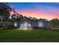 Charming home showcasing a lush front lawn, brick-paved entrance, and gray facade, set against a vibrant sunset sky at 571 Masalo Pl, Lake Mary, FL 32746