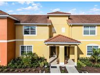 Inviting yellow townhouse featuring a well-kept lawn and a charming tile roof at 8939 Bismarck Palm Rd, Kissimmee, FL 34747
