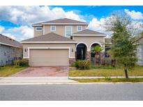 Two-story house with tan siding, a two-car garage, and a brick paver driveway at 285 Miro Dr, Davenport, FL 33837