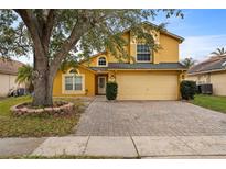 Two-story yellow house with a brick driveway and large tree at 11944 Cheltinham Dr, Orlando, FL 32824