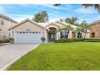 Tan house with white garage door, landscaping, and paver driveway at 4253 Willow Bay Dr, Winter Garden, FL 34787