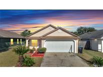 Tan house with white garage door, red walkway, and landscaping at 6433 Livewood Oaks Dr, Orlando, FL 32818
