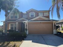 Two-story house with tan exterior, two-car garage, and landscaping at 115 Essex Pl, Davenport, FL 33896