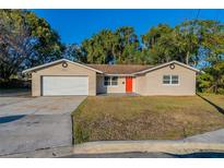 Tan single story house with a red door, attached garage, and well-maintained lawn at 5711 Bolling Dr, Orlando, FL 32808