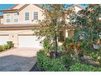 Tan three-story townhome with two-car garage, landscaping, and brick driveway at 8737 The Esplanade # 65, Orlando, FL 32836