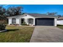 White house with black accents, a two-car garage, and a landscaped lawn at 1613 Lansfield Ave, Deltona, FL 32738