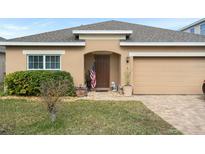 One-story house with tan exterior, American flag, and landscaped front yard at 2204 Napone Ln, Minneola, FL 34715