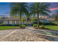 Charming home exterior with lush landscaping, brick driveway, and towering palm trees at sunset at 5737 Masters Blvd, Orlando, FL 32819