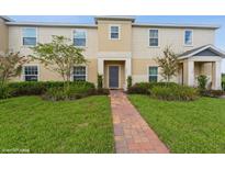 Two-story tan house with a gray door, brick pathway, and well-manicured lawn at 374 Annabelle Way, Davenport, FL 33837