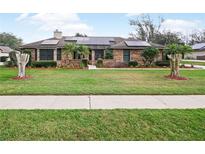 Charming brick home featuring manicured lawn, decorative trees and solar panels on the roof at 647 Saranac Dr, Winter Springs, FL 32708