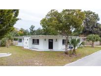 Charming mid-century modern home with white exterior, landscaping, and a black door at 25335 Troon Ave, Sorrento, FL 32776