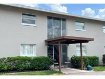 Two-story condo building featuring an entrance area with a canopy and chairs, surrounded by well-maintained landscaping at 5885 Dahlia Dr # 30/215, Orlando, FL 32807