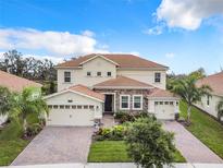 Stunning two-story home with a tile roof, lush landscaping, and a brick-paved driveway leading to a three-car garage at 8886 Fallen Oak Dr, Davenport, FL 33896