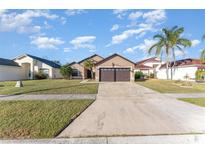 Tan house with brown double garage door, green lawn, and palm trees at 2463 Hybrid Dr, Kissimmee, FL 34758