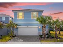 Two-story light blue house with a white garage door and landscaping at 7260 Oakmoss Loop, Davenport, FL 33837