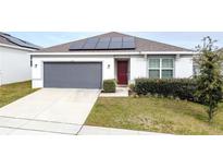 One-story house with gray garage door and solar panels at 1623 Aspen Ave, Davenport, FL 33837