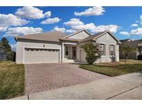 One-story home with a beige exterior, a two-car garage, and a brick paver driveway at 219 Blue Cypress Dr, Groveland, FL 34736