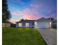 Gray house with white garage door, landscaped lawn, and a pink and purple sunset in the background at 255 Autumn Ridge Rd, Deltona, FL 32725