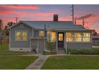 Charming gray bungalow-style house with a metal roof, brick chimney, and inviting front porch with an adjacent garden bed at 2250 W County Road 44, Eustis, FL 32726