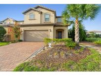 Two-story house with tan siding, brick driveway, and landscaping at 5452 Misty Oak Cir, Davenport, FL 33837